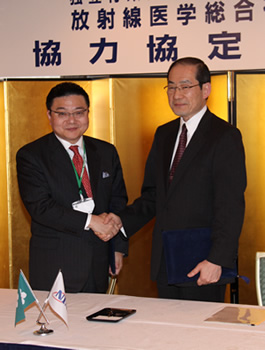 調印式を終え、握手する古川康佐賀県知事(左)と米倉義晴放医研理事長
